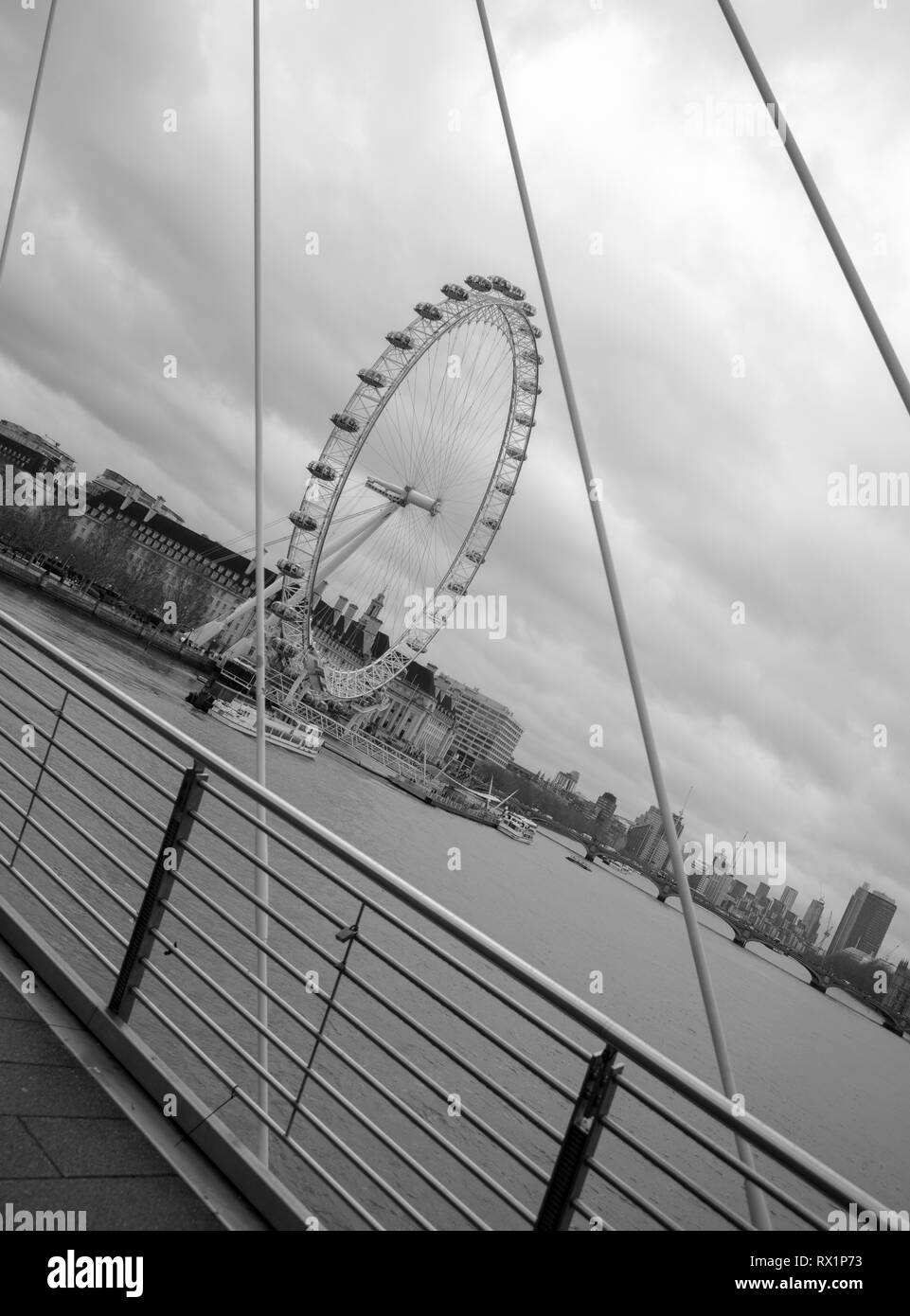View of London Eye through the steel rods of one of the pedestrian Golden Jubilee Bridges, on a cold and blustery day in March. Stock Photo