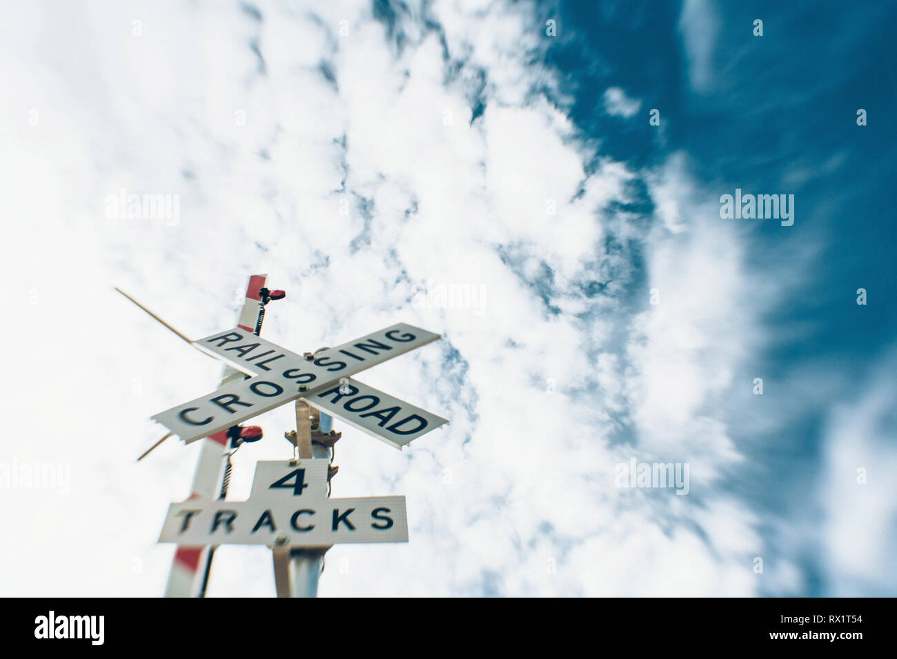 Low angle view of railroad track and crossing sign against cloudy sky Stock Photo