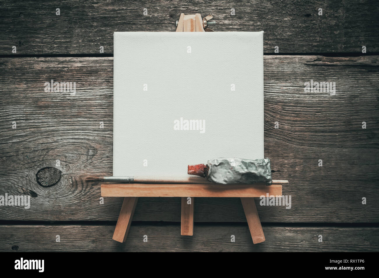 Canvas on easel, paint tube and paintbrush. Old wooden background. Top view. Flat lay. Copy space for text. Stock Photo