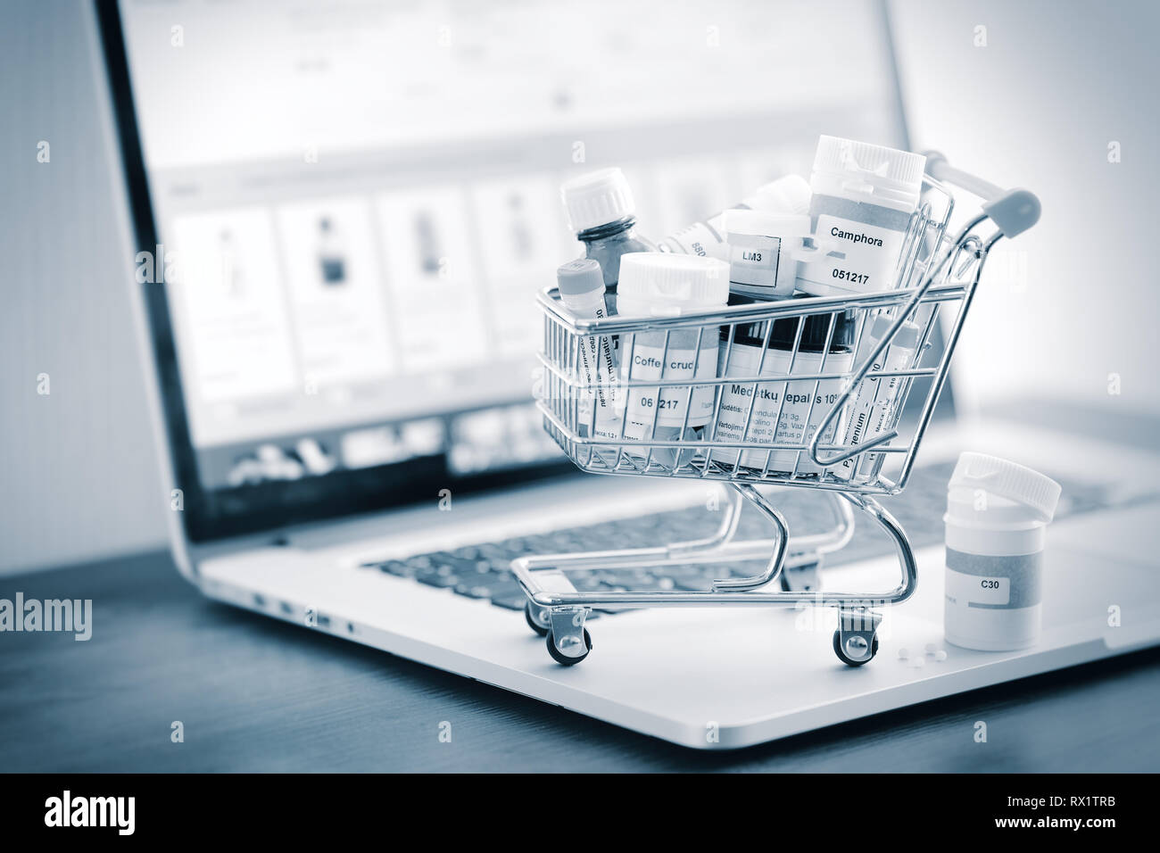 Mini shopping cart full of homeopathic remedies on laptop background. Homeopathy and internet online shopping concept. Black and white stylized. Stock Photo