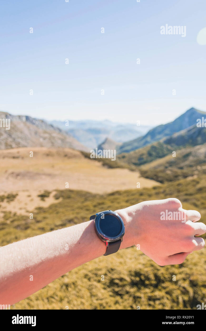 Cropped hand of man checking time on mountain against clear sky during sunny day Stock Photo