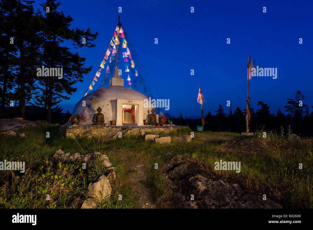 A Buddhist Stupa with prayer flags blowing in the wind are lit up at night at a retreat on Cortes Island,  Cortes Island, British Columbia, Canada Stock Photo