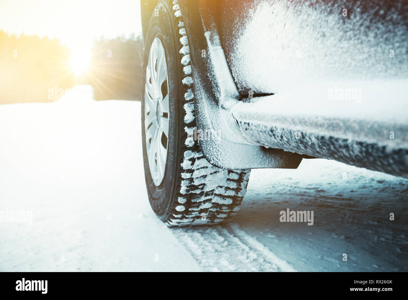 Car tires covered with snow on winter road through forest at sunny day. Stock Photo