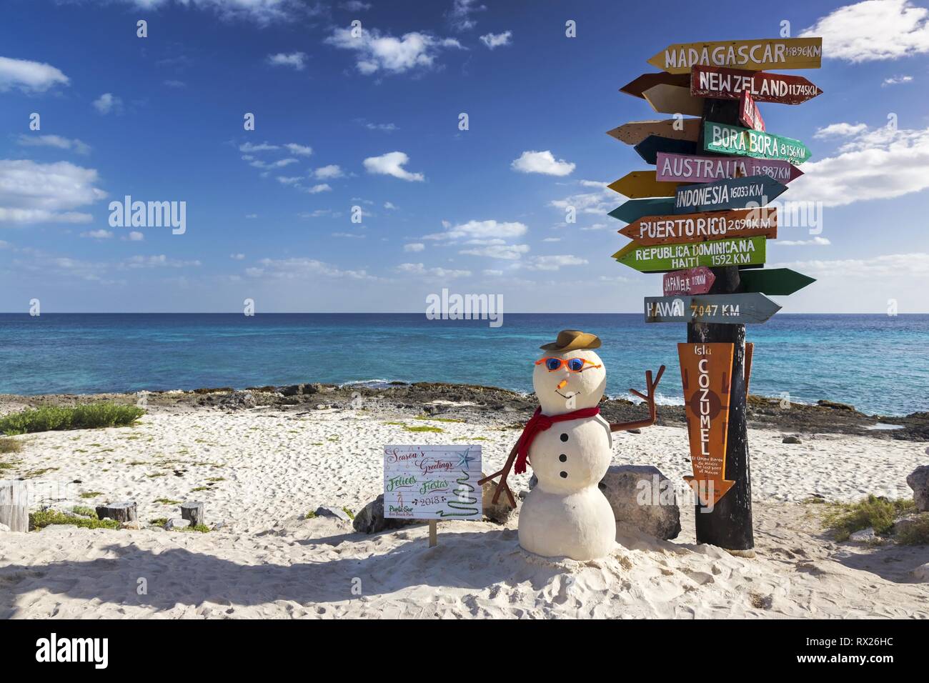 Post Sign with directions to World travel destinations and Isolated Christmas Snowman on Sandy Beach Punta Sur Ecological Reserve in Cozumel, Mexico Stock Photo