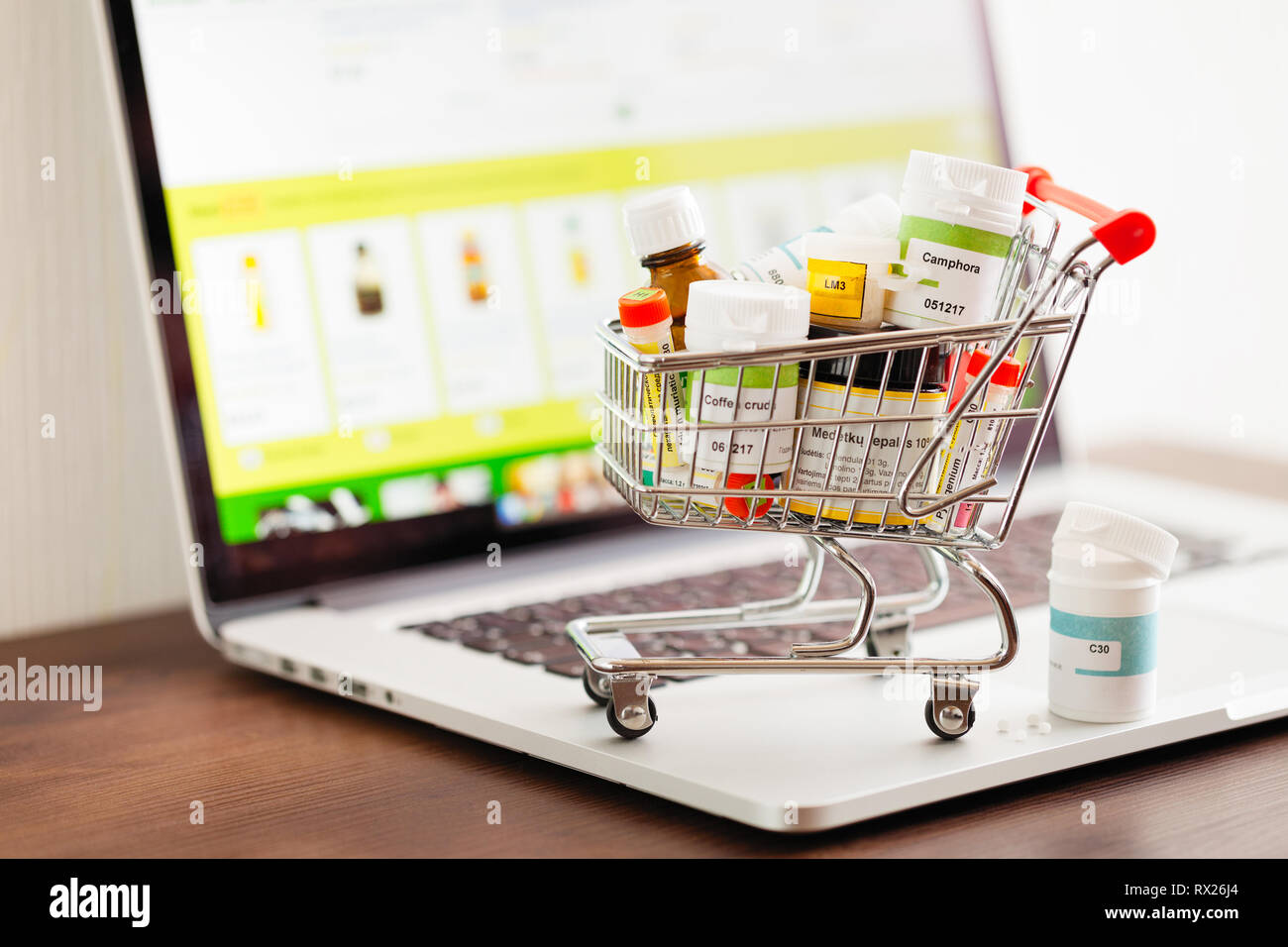 Mini shopping cart full of homeopathic remedies on laptop background. Homeopathy and internet online shopping concept. Stock Photo