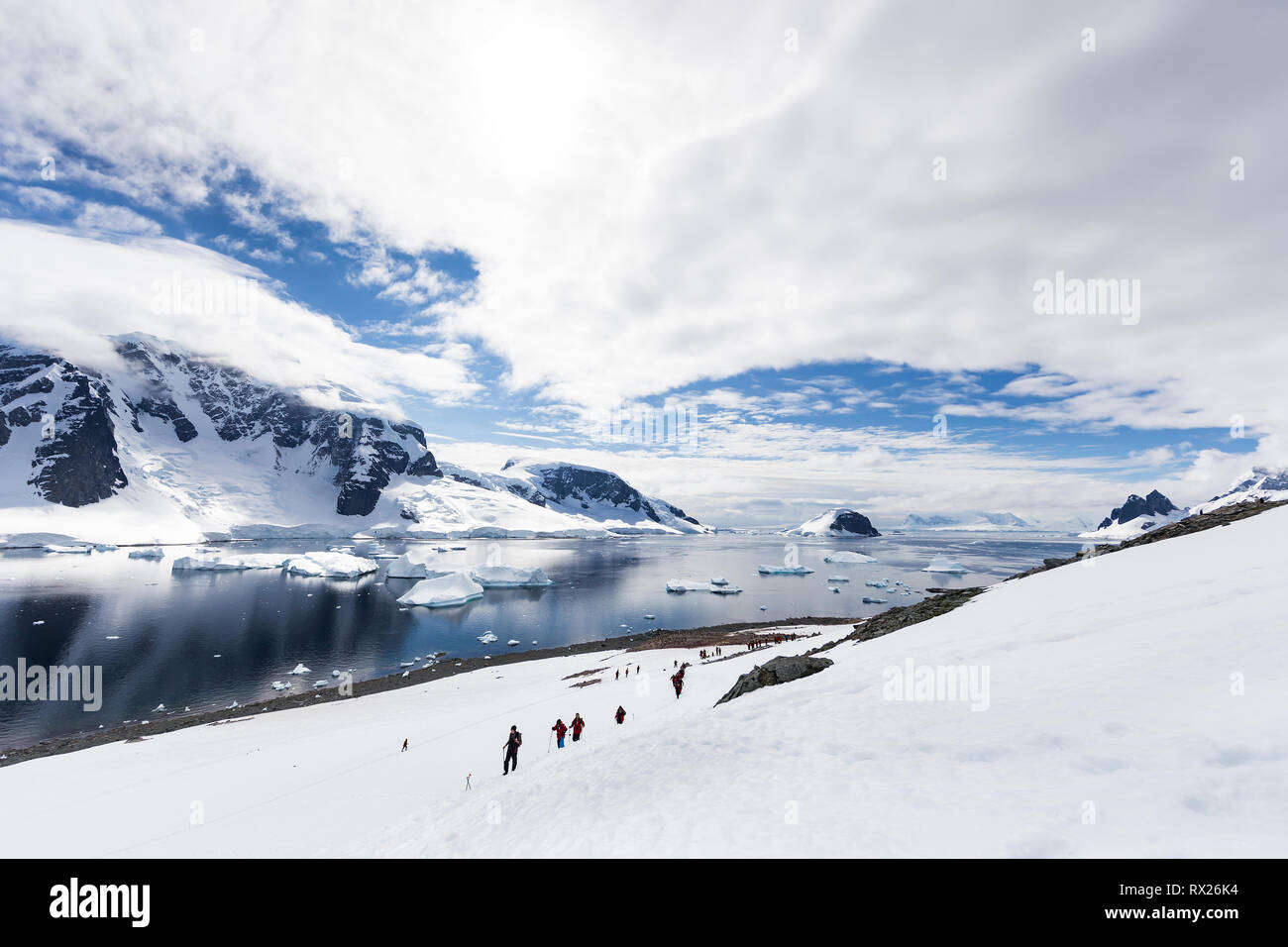 Visitors to Danco Island hike up a snowfield against a backdrop of icebergs and glaciers.  Danco Island, Antarctic Peninsula, Antarctica Stock Photo