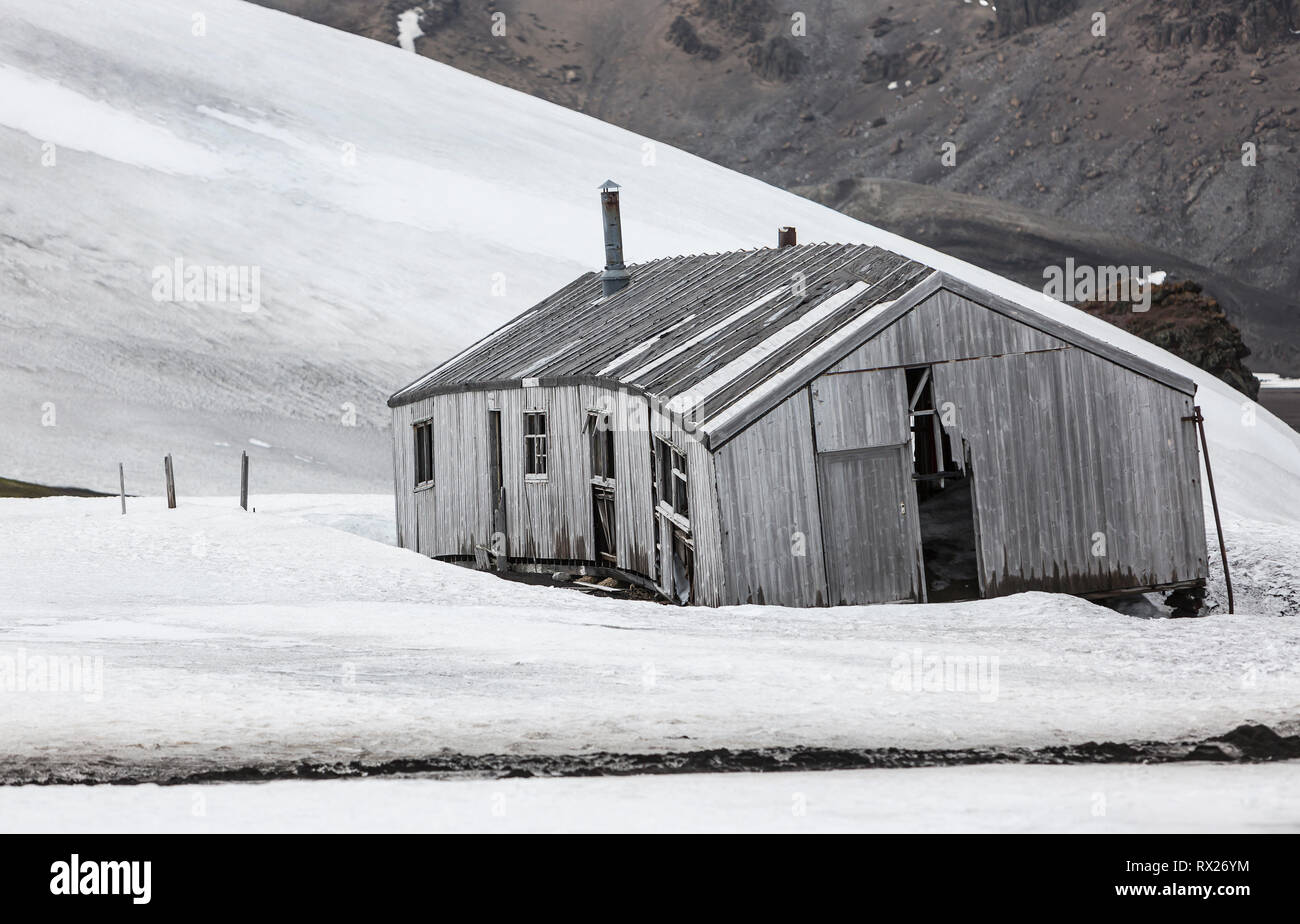 An abandoned bunkhouse amongst a snowfield slowly deteriates in the harsh climate of Whalers Bay.  Deception Island, South Shetland Islands, Antarctica. Stock Photo