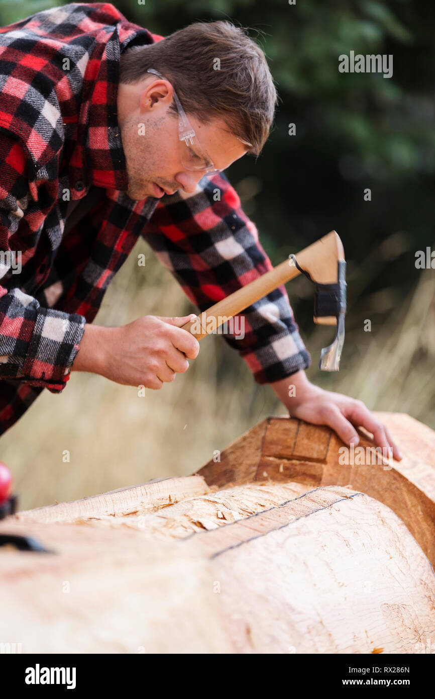 A young first nations carver uses his adze to form out a design element on a totem pole, Comox, The Comox Valley, Vancouver Island, British Columbia,  Stock Photo