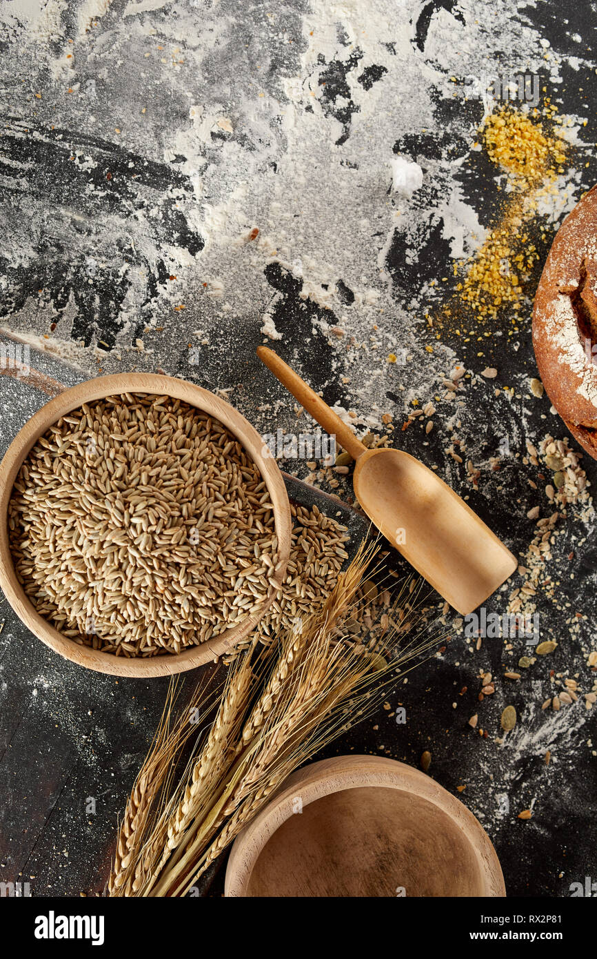 Still life with ears of golden wheat, seeds and flour in rustic wooden bowl on a messy kitchen table with copy space viewed from above Stock Photo