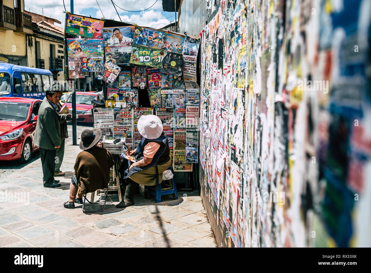 Customers and vendors around a paper and magazine stall on the street by a wall covered with posters. (Cusco, Peru) Stock Photo