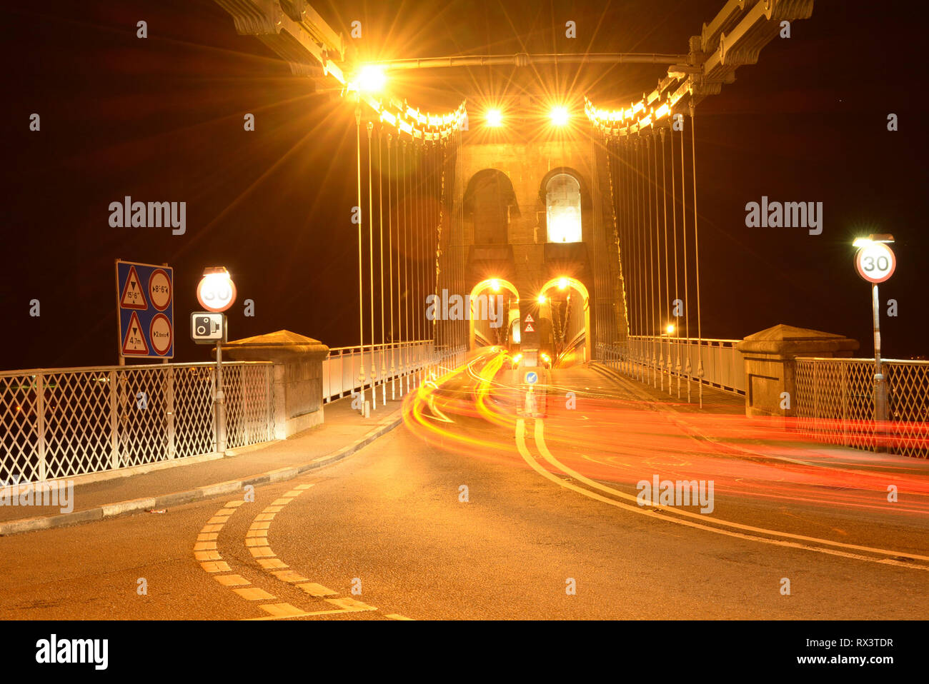 Tail lights of cars as they travel over the Menai Suspension Bridge to Anglesey in North Wales at night time. Stock Photo