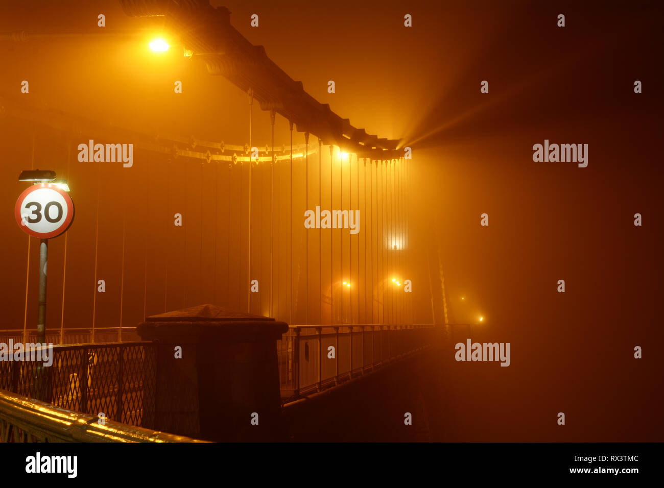 Misty and Foggy Menai Suspension Bridge at night time. This bridge joins the Welsh mainland with the beautiful Isle of Anglesey. Stock Photo