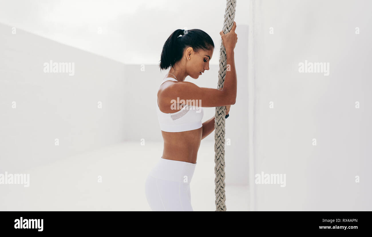 Girl Standing With Rope Side view of a woman in fitness wear standing holding a rope. Athletic ...