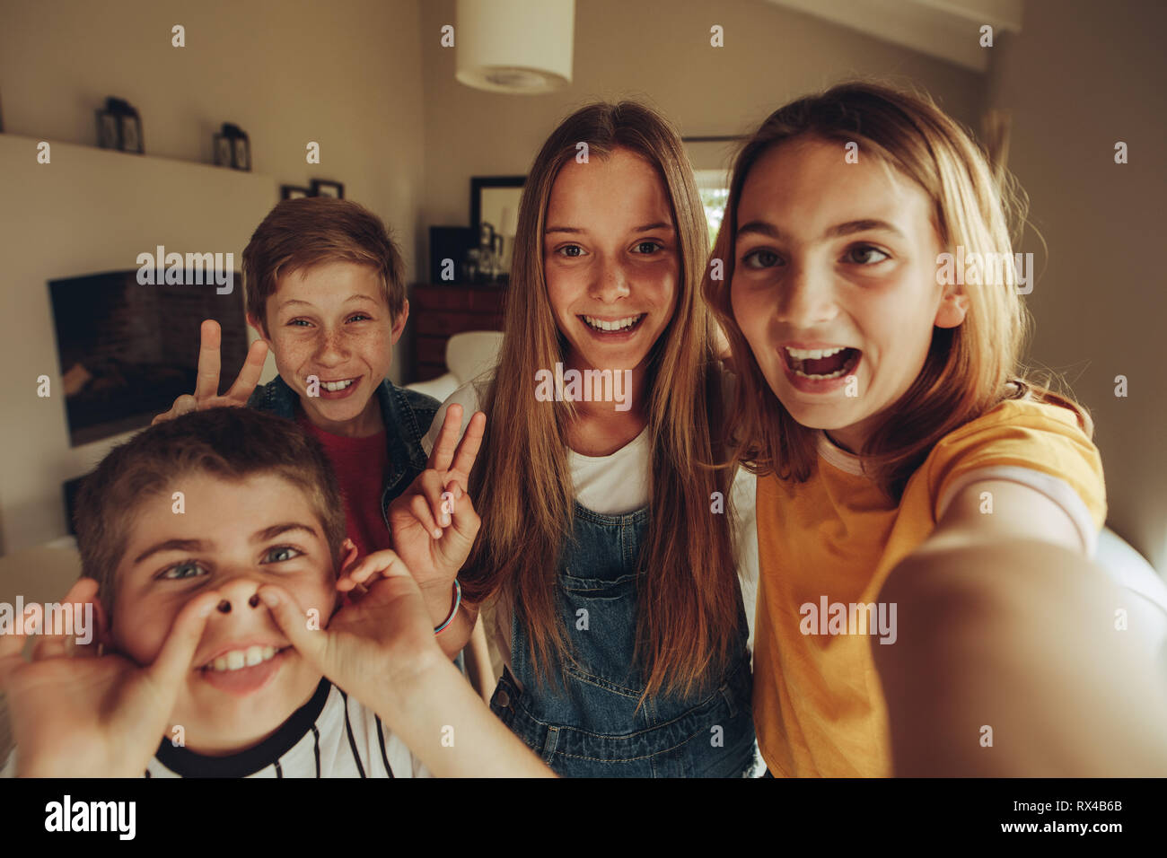 Cheerful kids making funny faces and showing victory sign while taking a selfie. Kids enjoying their time having fun at home. Stock Photo