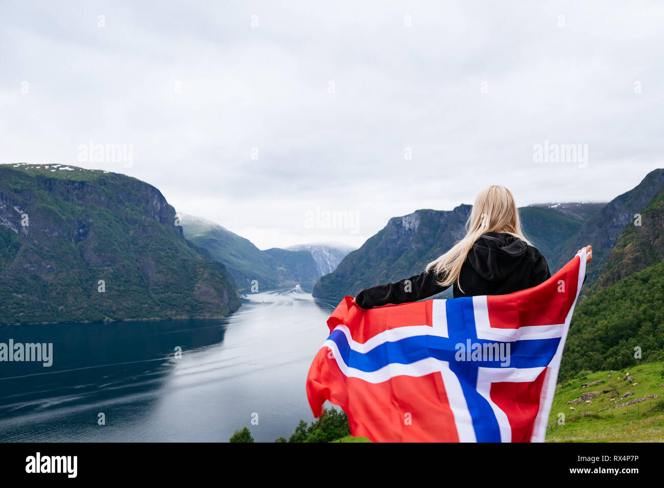 Panorama of Aurlandsfjord. Tourist girl with the flag of Norway enjoys a beautiful view of the fjord and mountains Stock Photo