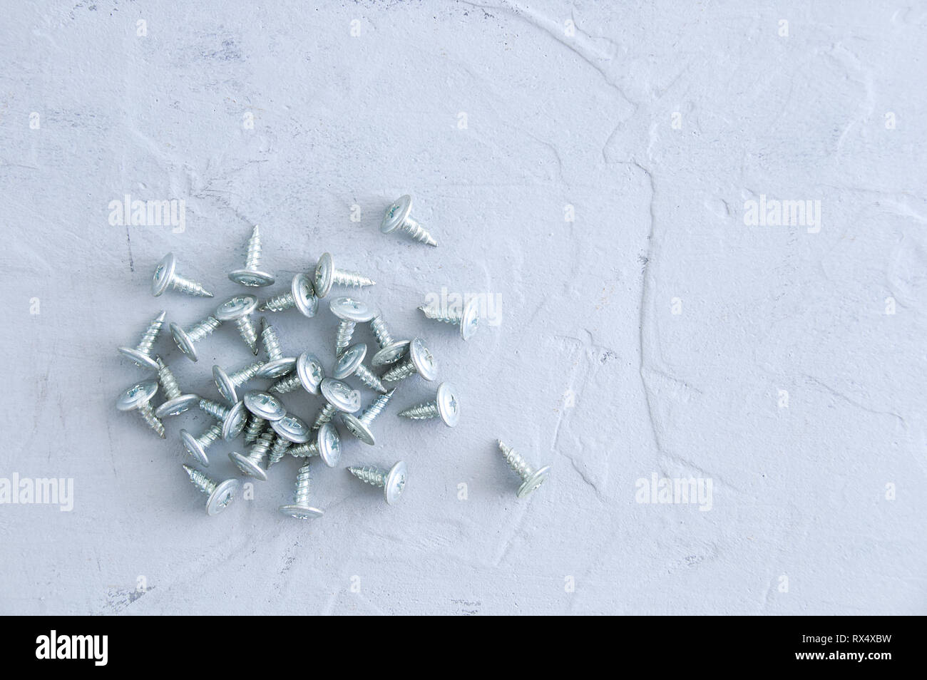 Silvery metal screws for plasterboard walls. On a gray concrete background. Close-up. Stock Photo