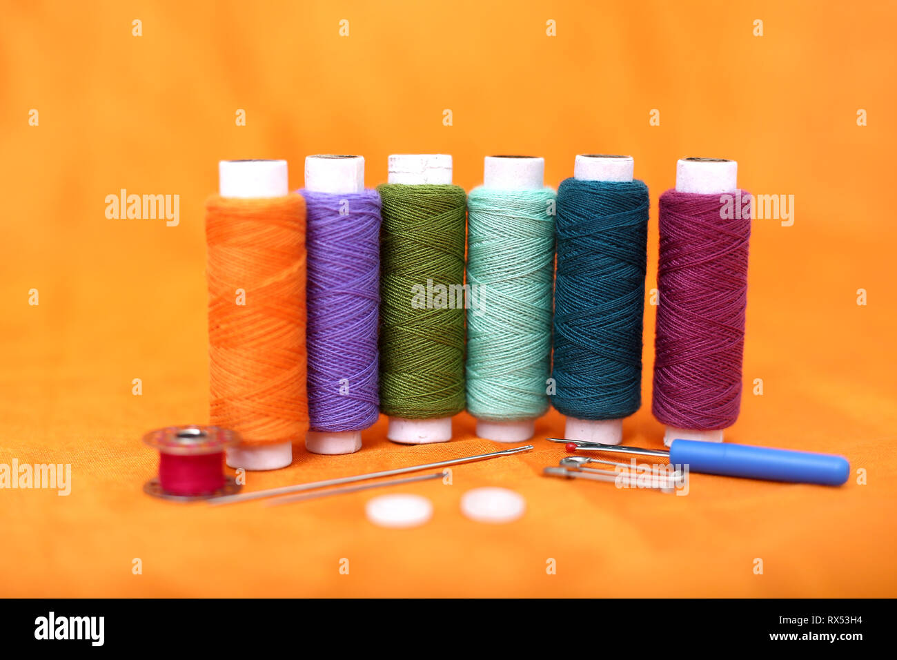 Photo of multicolored thread, needle, bobbin, button, safety pin and