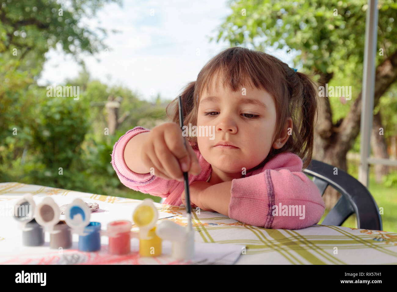 Cute little girl paints animal figures. Summer sunny day in the garden ...