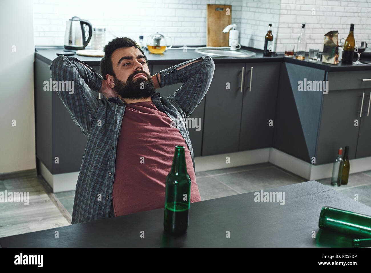 Drinking trouble. Depressed bearded man sits at the table with beer bottle in front of him. He is thinking about problems at work and troubles in rela Stock Photo