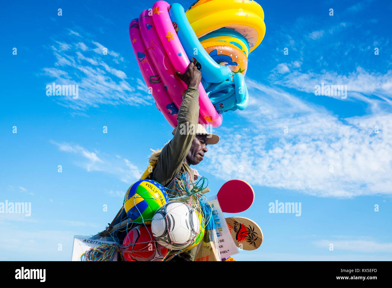 RIO DE JANEIRO - FEBRUARY 5, 2017: A Brazilian beach vendor selling colorful beach toys and inflatables carries his merchandise along Ipanema Beach. Stock Photo