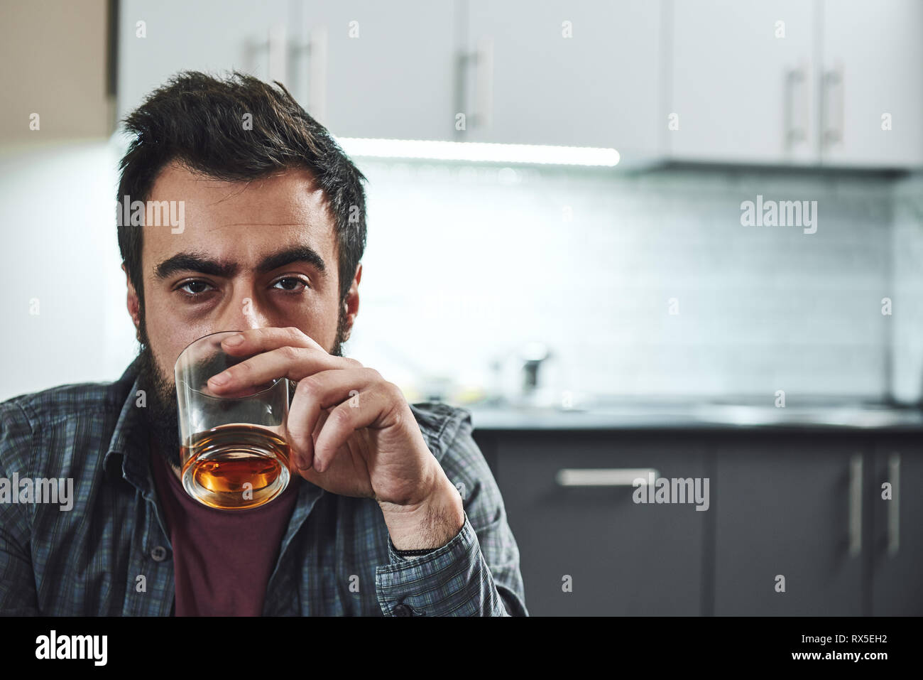 Drinking trouble. Depressed bearded man sits at the table with a glass of whiskey in his hand. He is thinking about problems at work and troubles in r Stock Photo