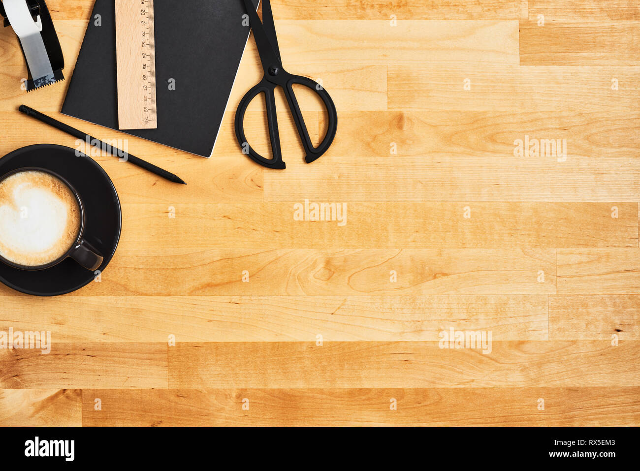 Black office or school supplies. Notepad, pencil, scissors, scotch tape and cup of coffee or cappuccino on yellow wooden table. Top view. Copy space f Stock Photo