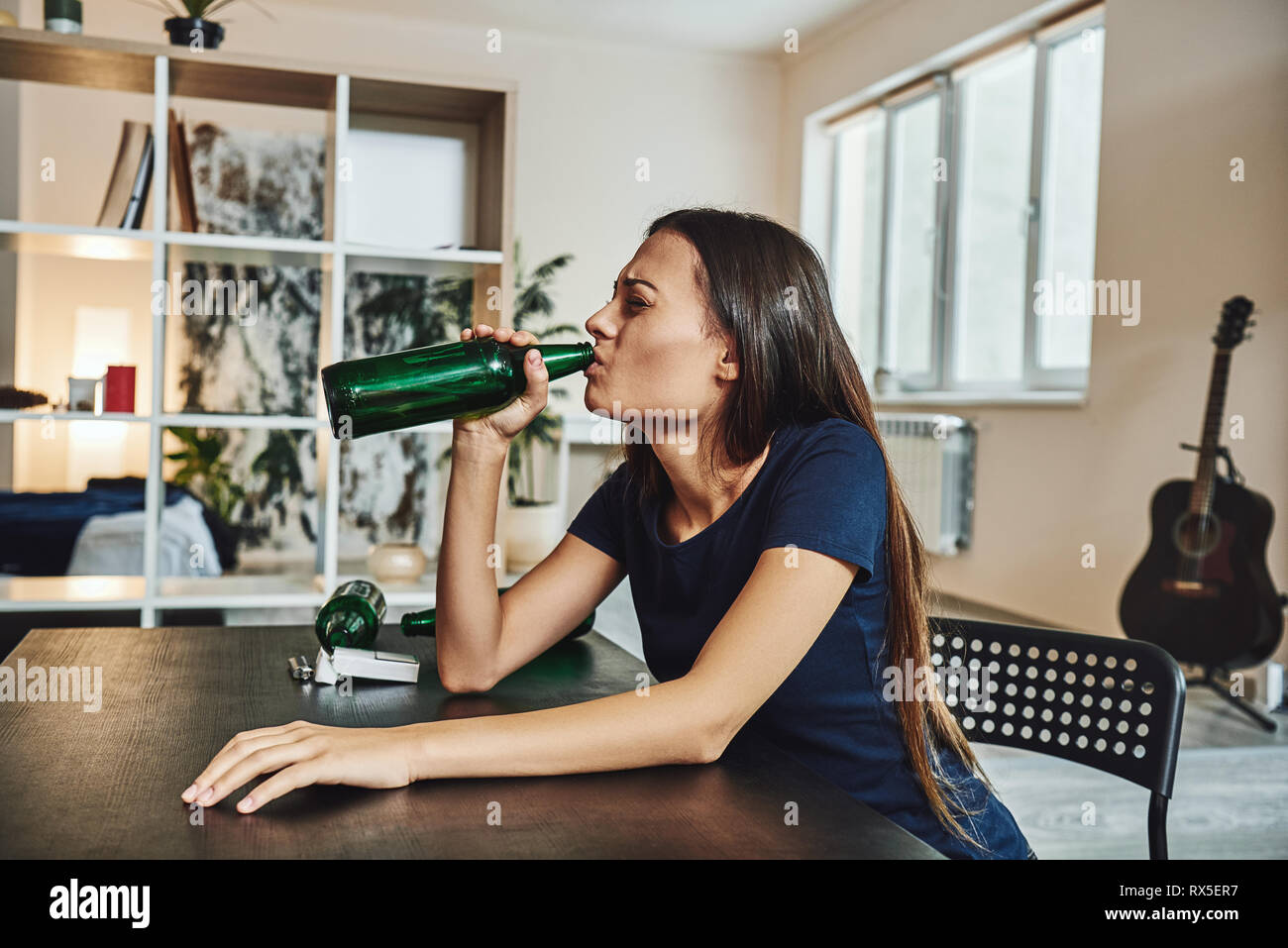 Depressed, divorced woman sitting alone at home and drinking beer from a bottle because of problems at work and troubles in relationships. Social and  Stock Photo