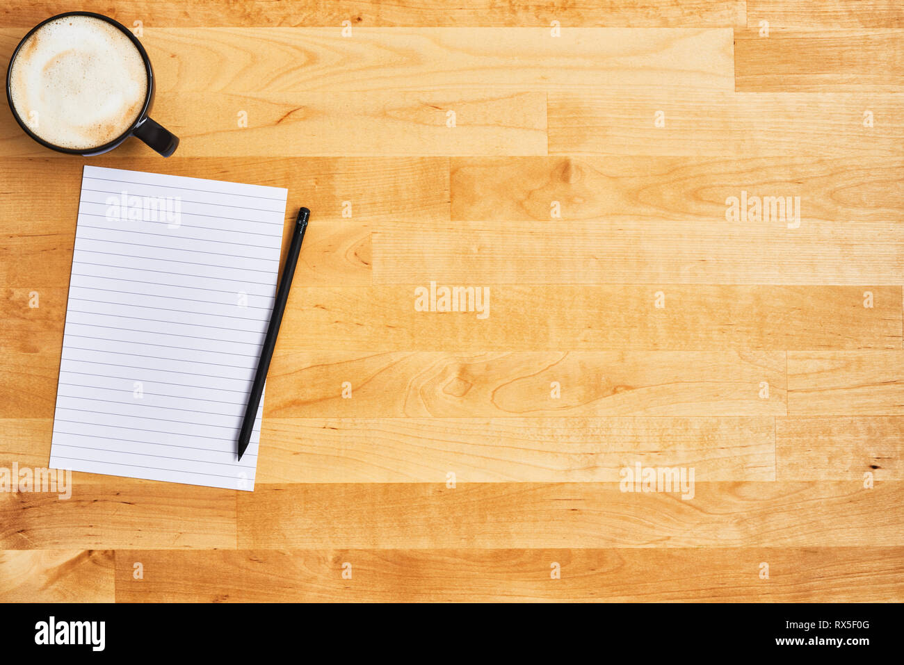 Cup of coffee or cappuccino with an empty sheet of paper and pencil on yellow wooden table. Top view. Copy space for text. Stock Photo