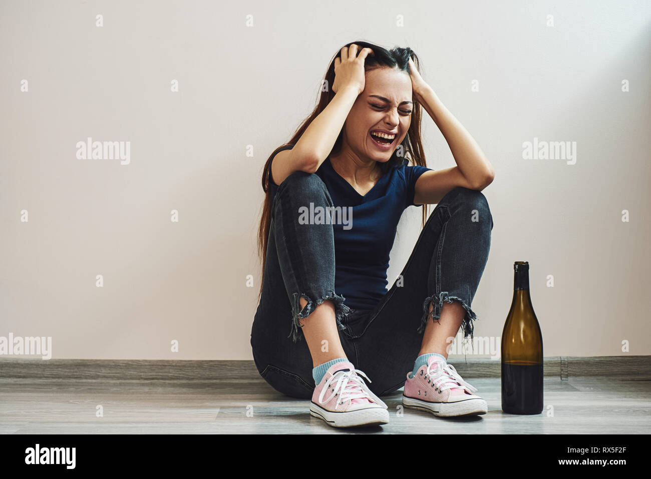 Sad dark-haired woman sitting on the floor with a bottle of red wine crying, divorce concept, parting, alcoholism. Horizontal shot Stock Photo