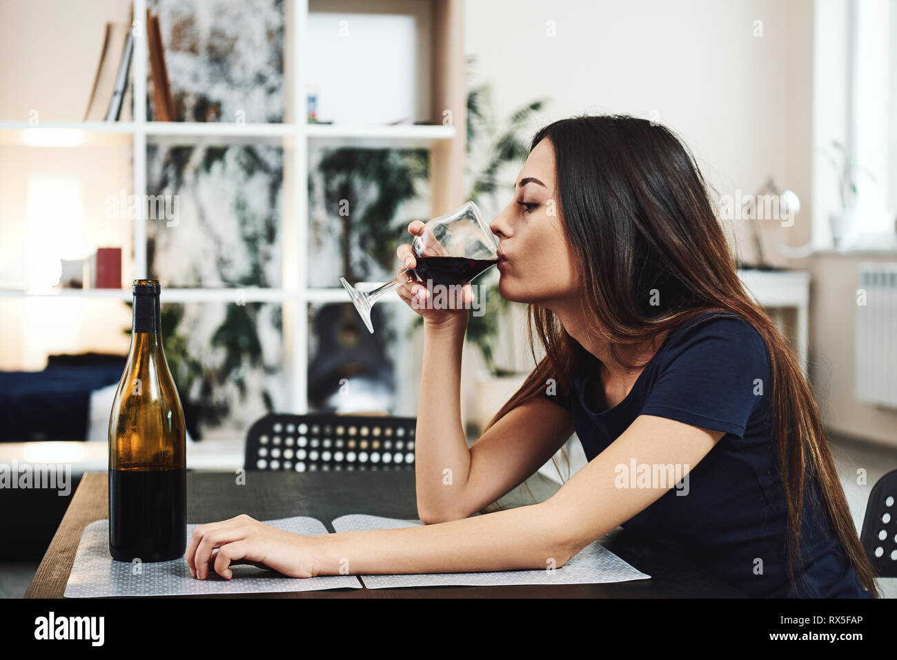 Depressed, divorced woman sitting alone at home and drinking a glass of red wine because of problems at work and troubles in relationships. Social and Stock Photo