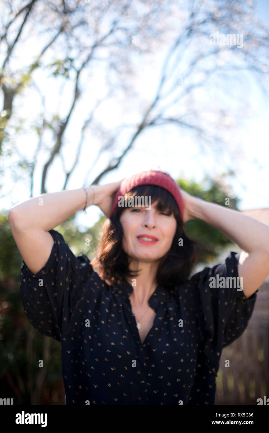 beautiful french woman with woolly hat and her hands behind her head, looking relaxed and happy about the advent of Spring Stock Photo