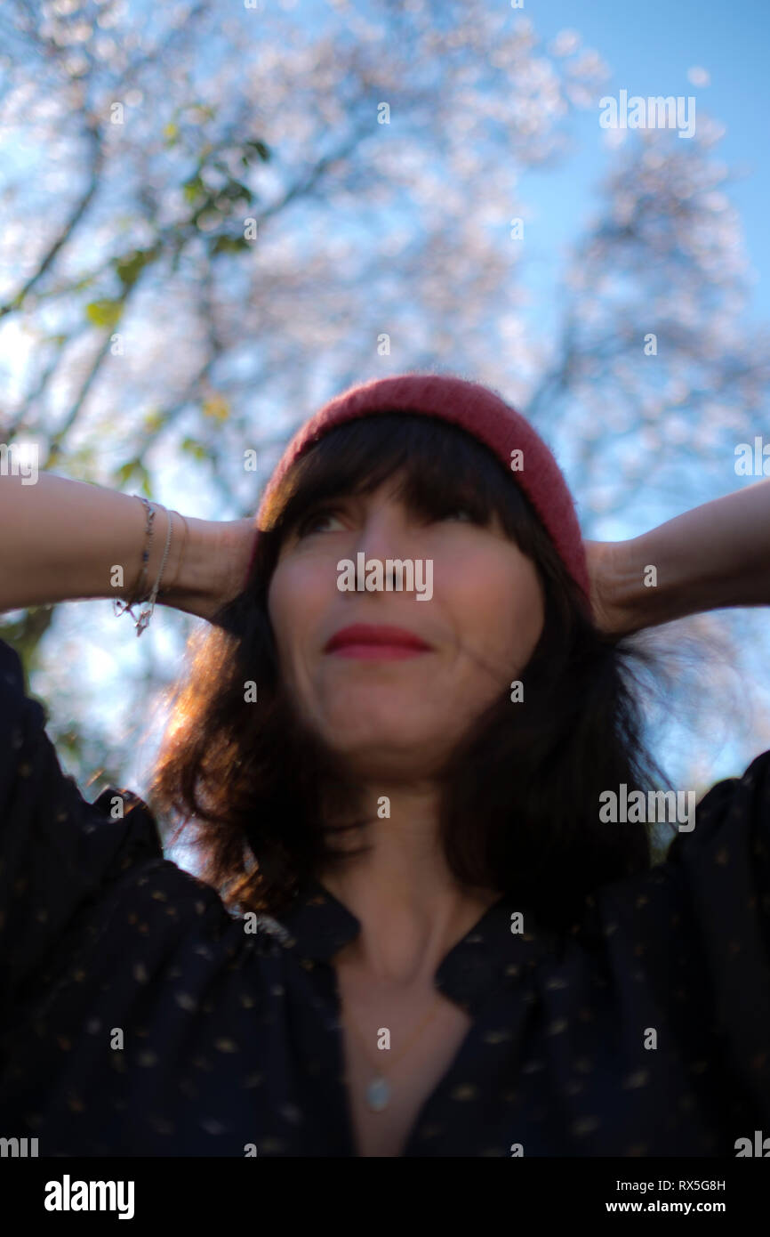 low angle close up of beautiful french woman with woolly hat and her hands behind her head, looking relaxed and happy about the advent of Spring Stock Photo