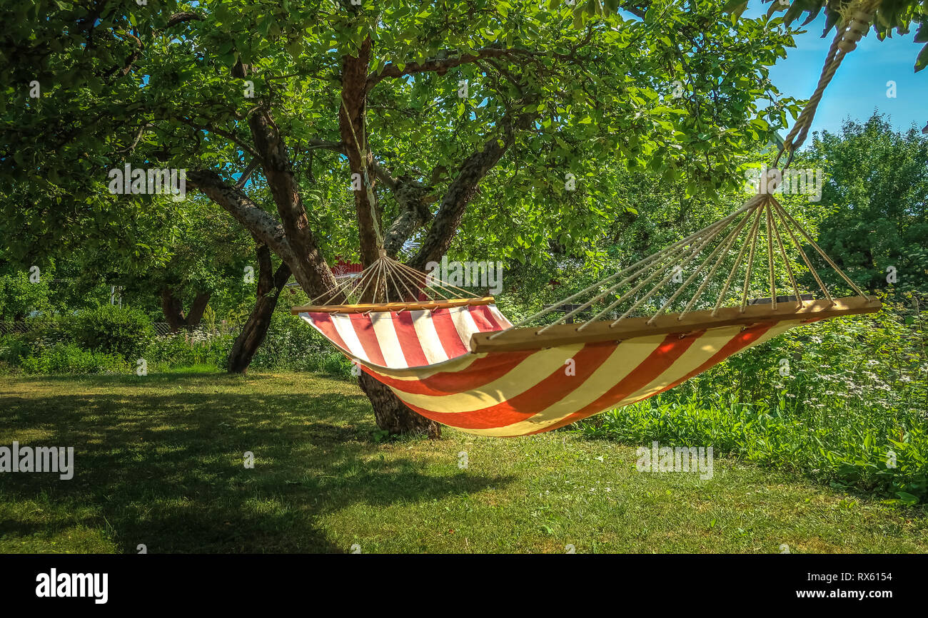 A striped hammock between two trees in a sunny green garden. Concept for holidays, summer vacation and lazy days. Stock Photo