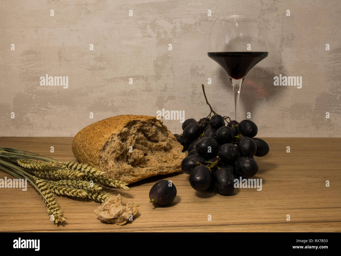 A wheat bread and shock of wheat with red grapes and glas of red wine as easter background Stock Photo