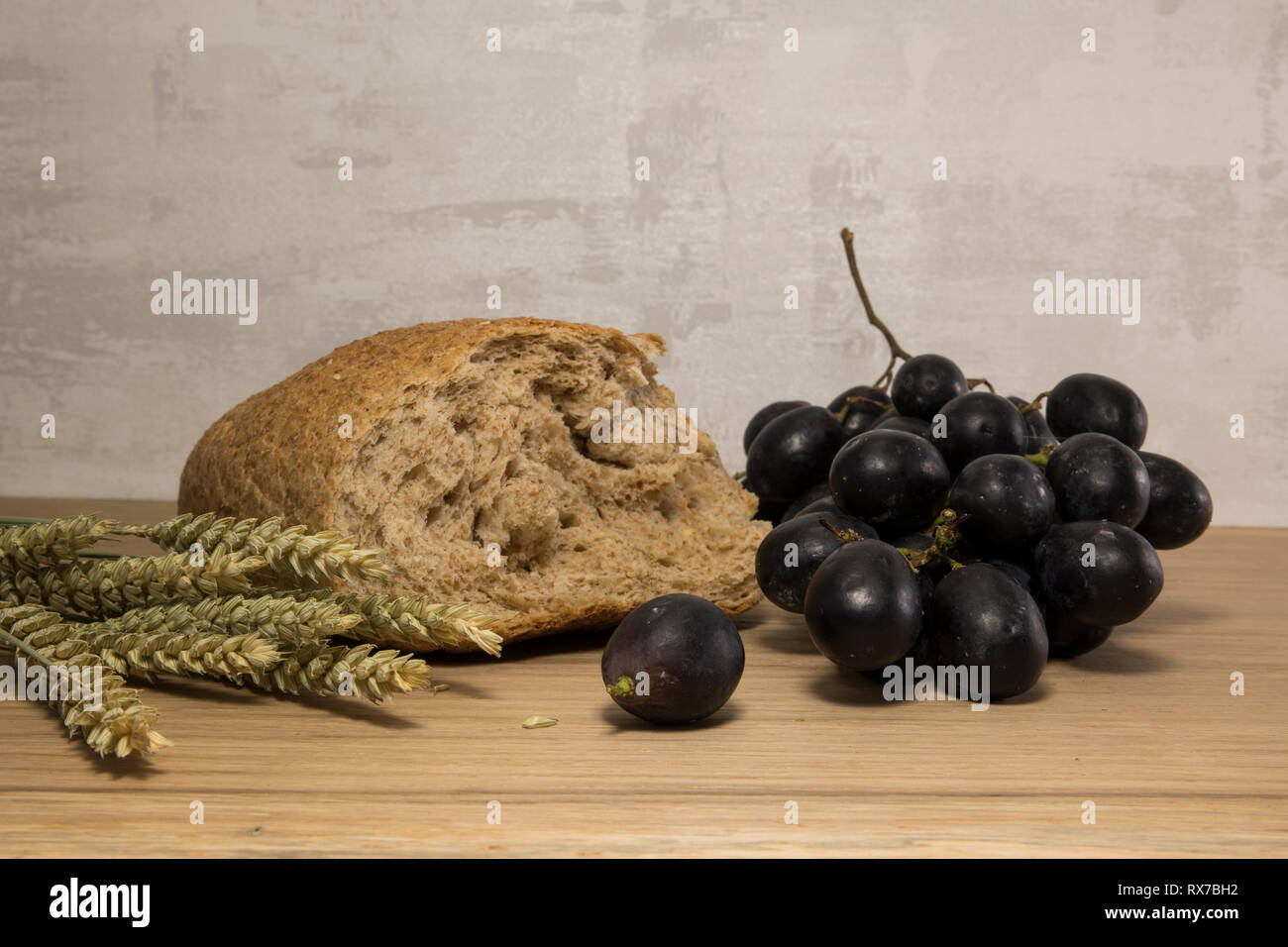 A wheat bread and shock of wheat with red grapes as easter lst supper background Stock Photo