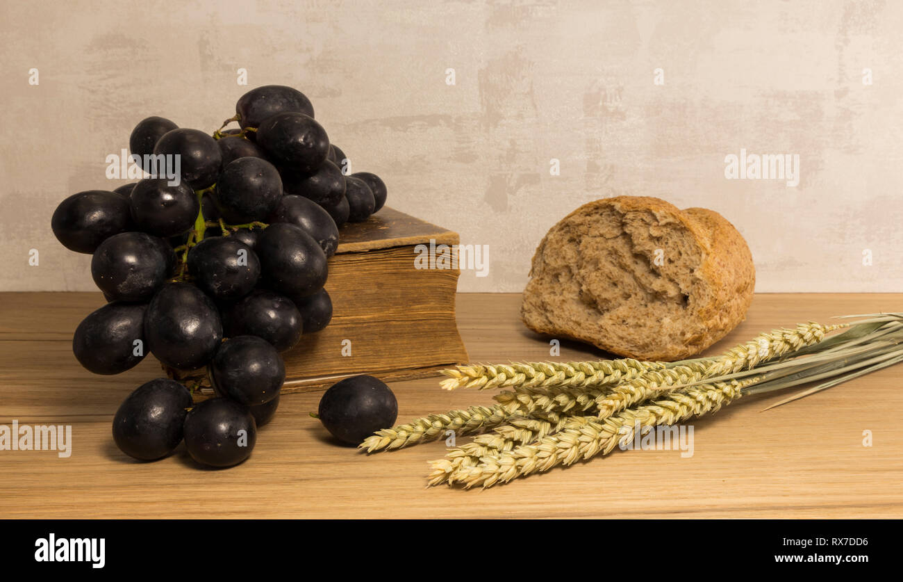 A wheat bread and shock of wheat with red grapes and and bible as easter background Stock Photo