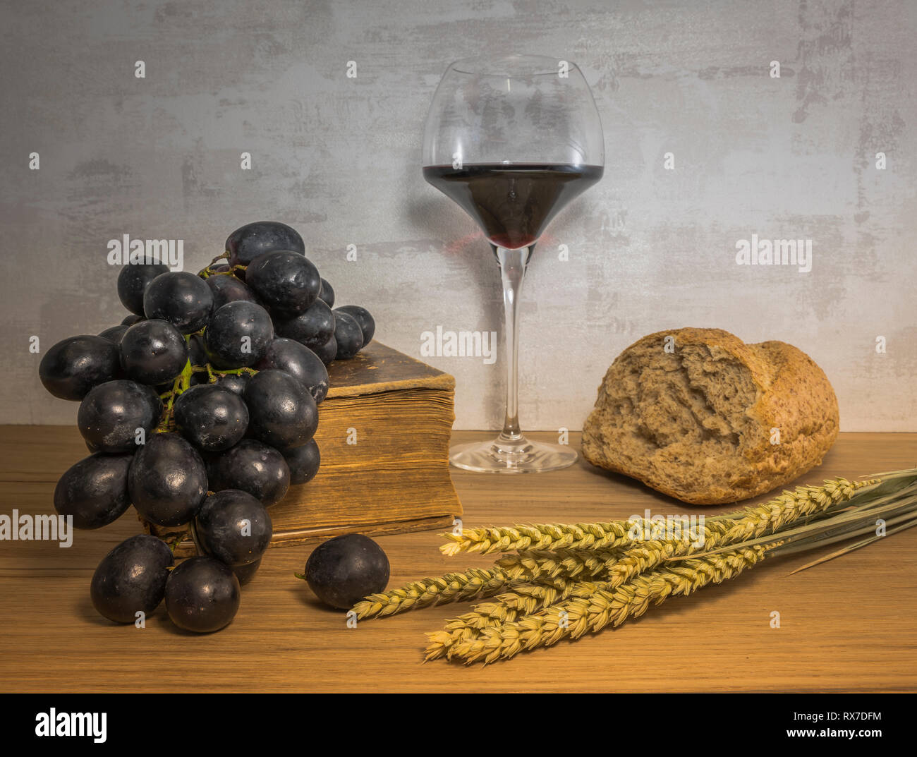 A wheat bread and shock of wheat with red grapes and glas of red wine and bible as easter background Stock Photo