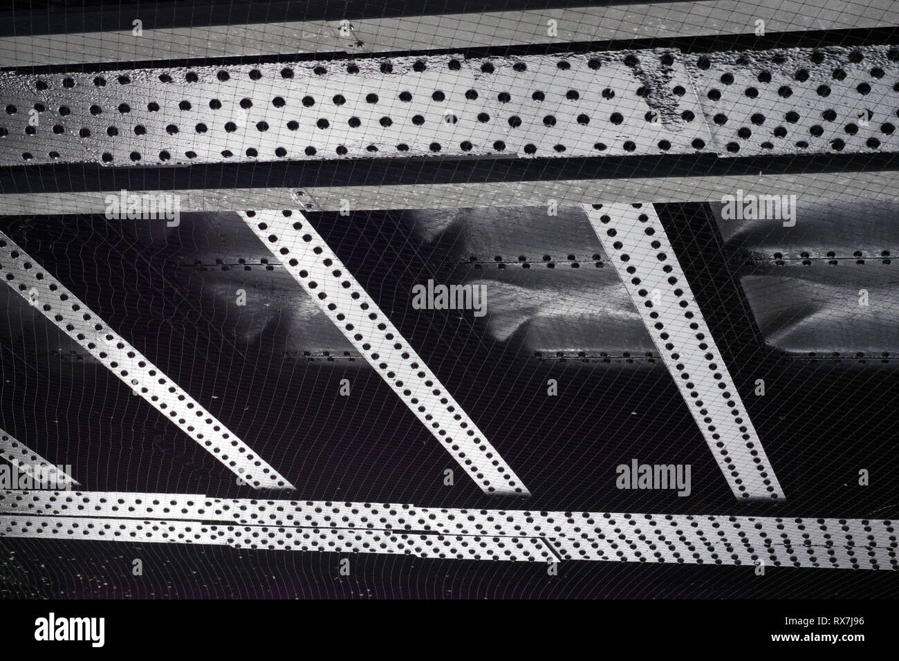 Underside of railway bridge showing riveted steel plates. Built to last. Fine mesh to stop pigeons. Stock Photo