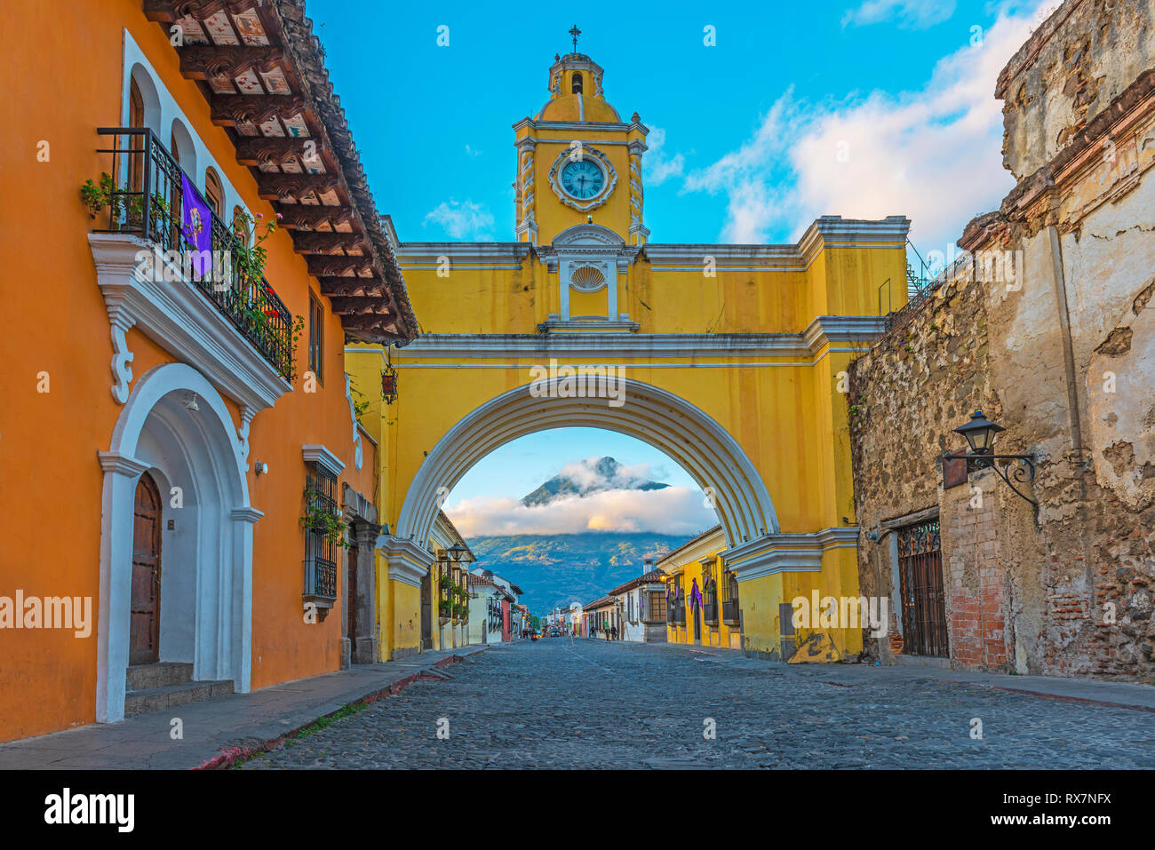 The Agua volcano illuminated by the first sunlight at sunrise with the main street of Antigua city and its yellow arch, Guatemala, Central America. Stock Photo