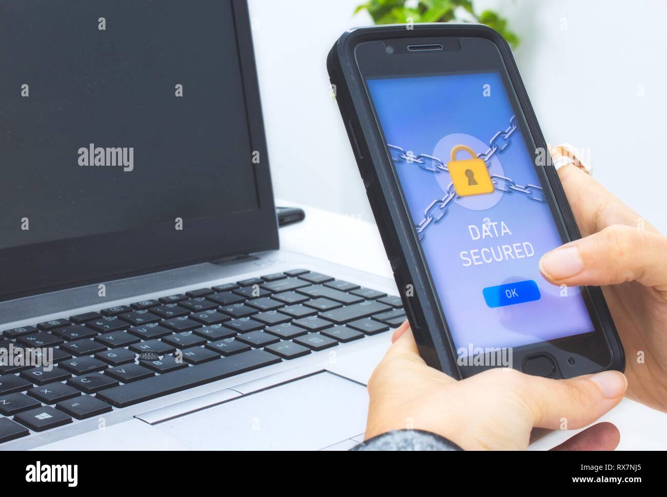 Woman holding a mobile smart phone with a data security application displaying a yellow padlock and pressing OK button with finger Stock Photo