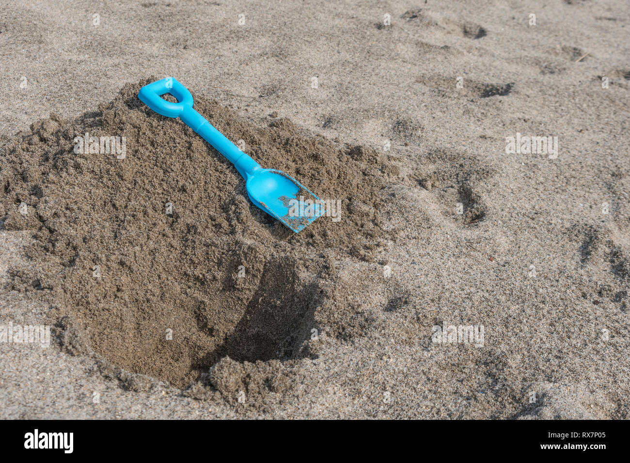 Seaside hole dug into sand, with kids blue spade. Metaphor 'dig a hole