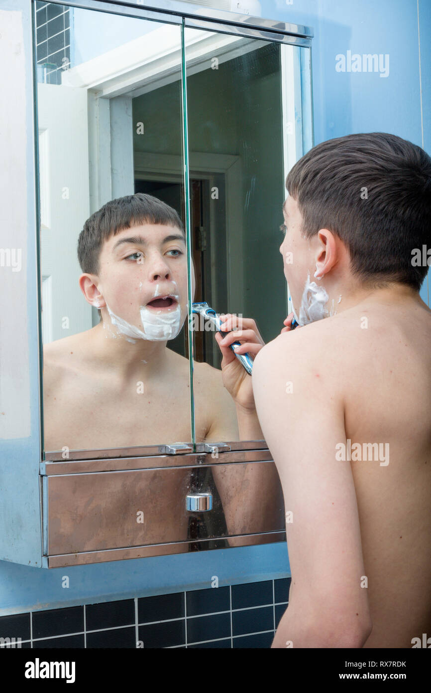 Teenage boy using a bathroom mirror to shave in the morning Stock Photo