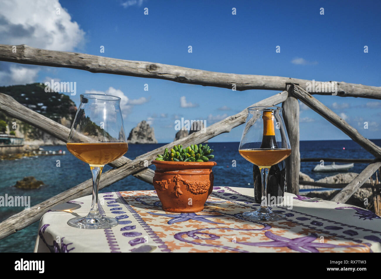 Pair of glasses of white wine and bottle with the Capri faraglioni in the background Stock Photo