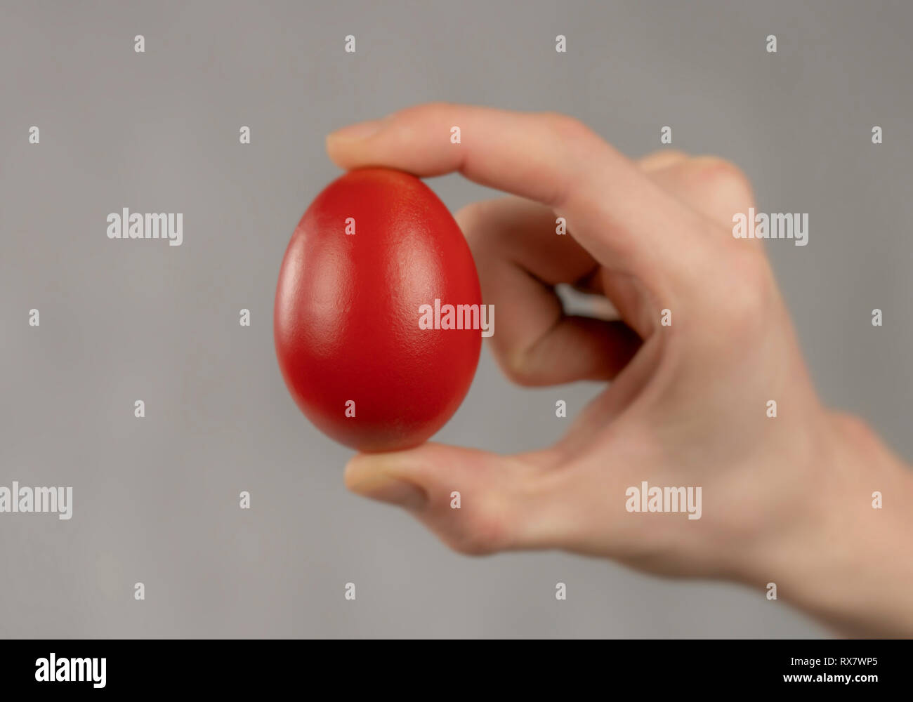 Easter red egg sandwiched between fingers on white abstract background Stock Photo Alamy