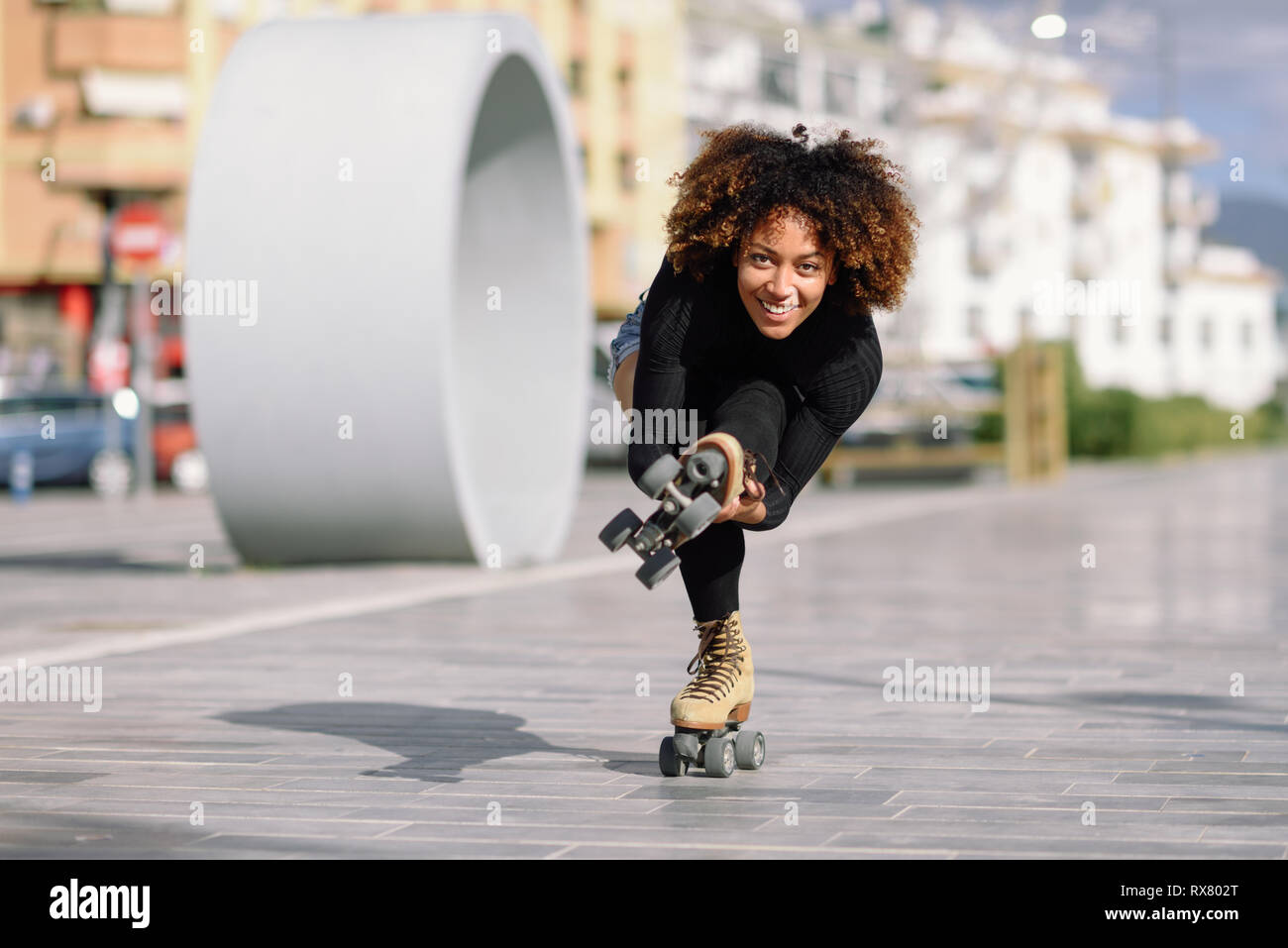 Black woman on roller skates riding outdoors on urban street Stock