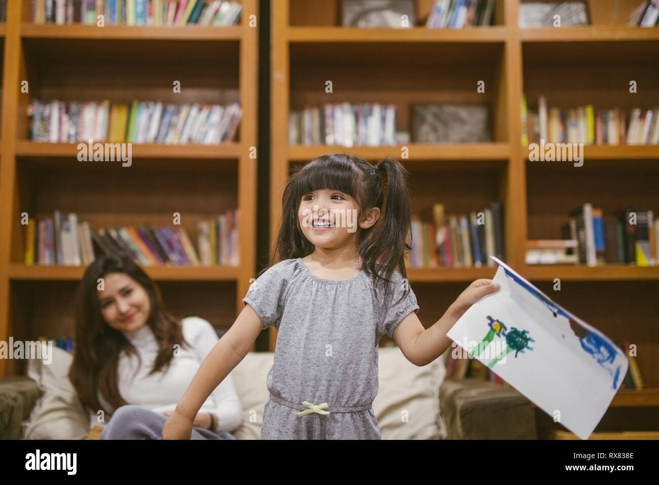 Cute little girl painting a picture with mother and show her work at home Stock Photo