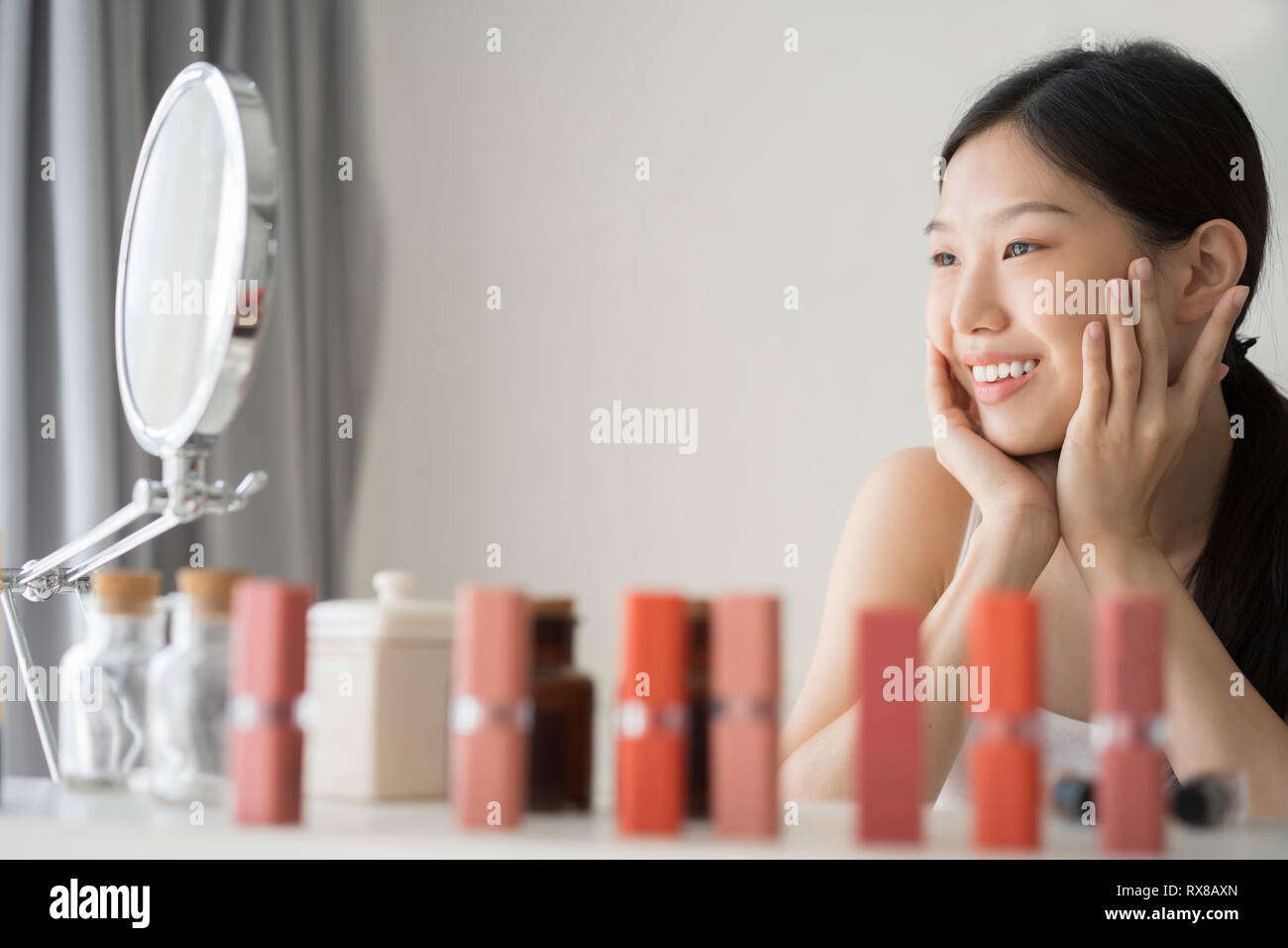 Female Skin Care. Young asian woman touching her face and looking to mirror. Stock Photo