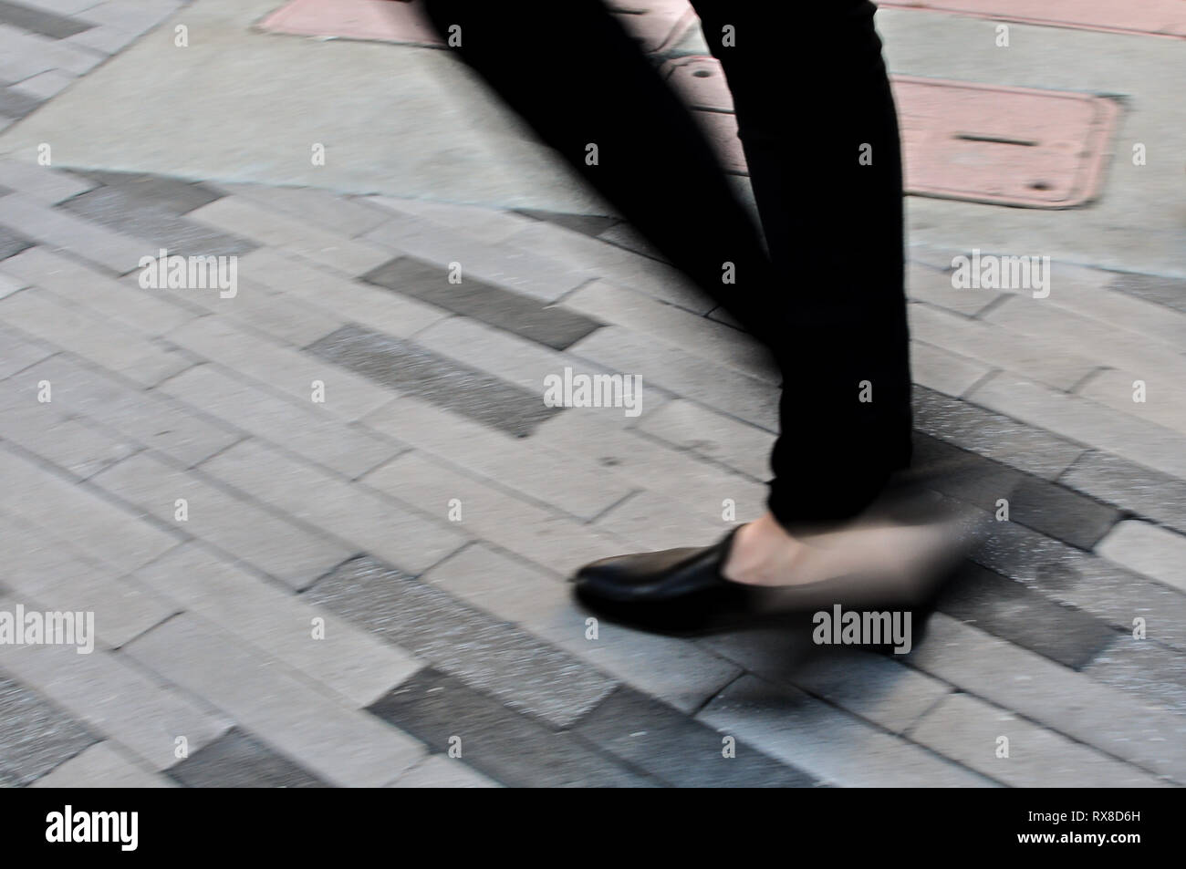 blurry close up lower legs and black shoe of person walking on cobble stone Stock Photo