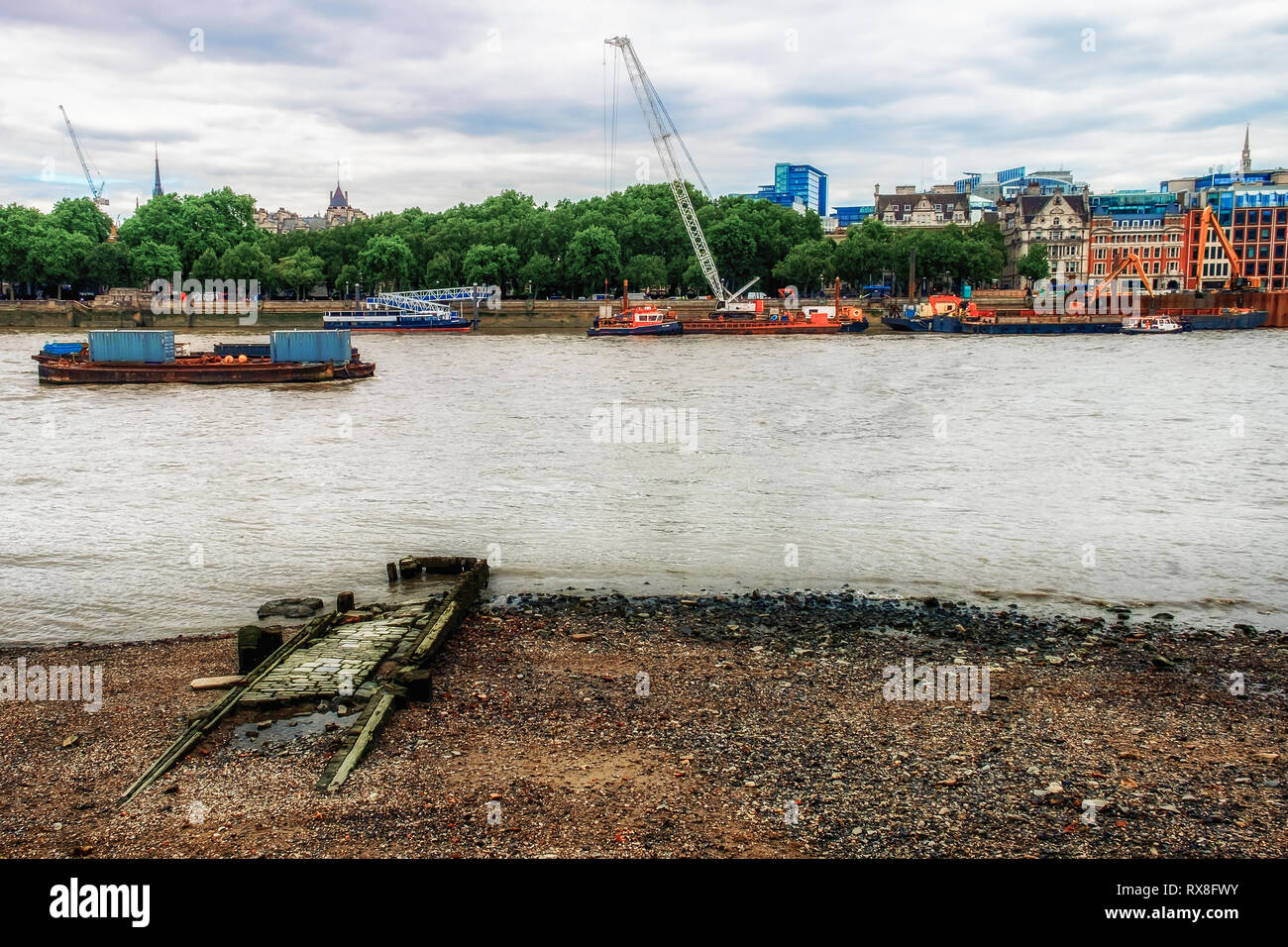 Derelict river taxi paved path on the South Bank of the River Thames at low tide,  facing North Bank under construction, London UK Stock Photo