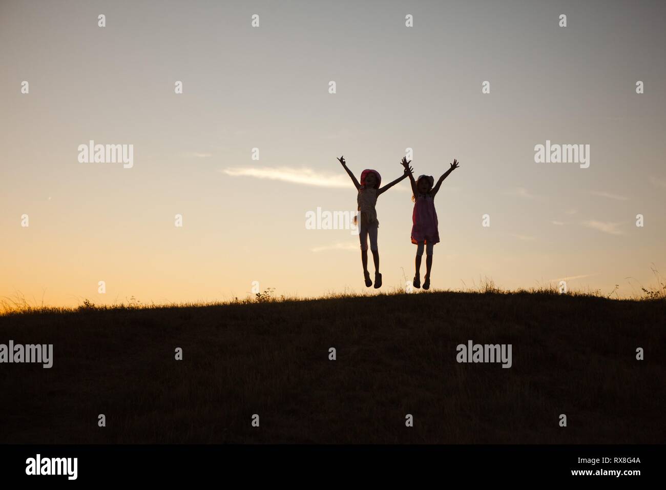 Two children jumped and raised hands up. Captured emotion during sunset after summer day. Stock Photo